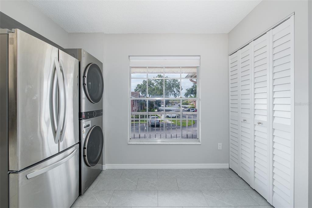 A laundry room with a stacked washer-dryer, stainless steel refrigerator, window, and white louvered closet doors — 4933 MYRTLE OAK DRIVE UNIT 23, NEW PORT RICHEY, FL