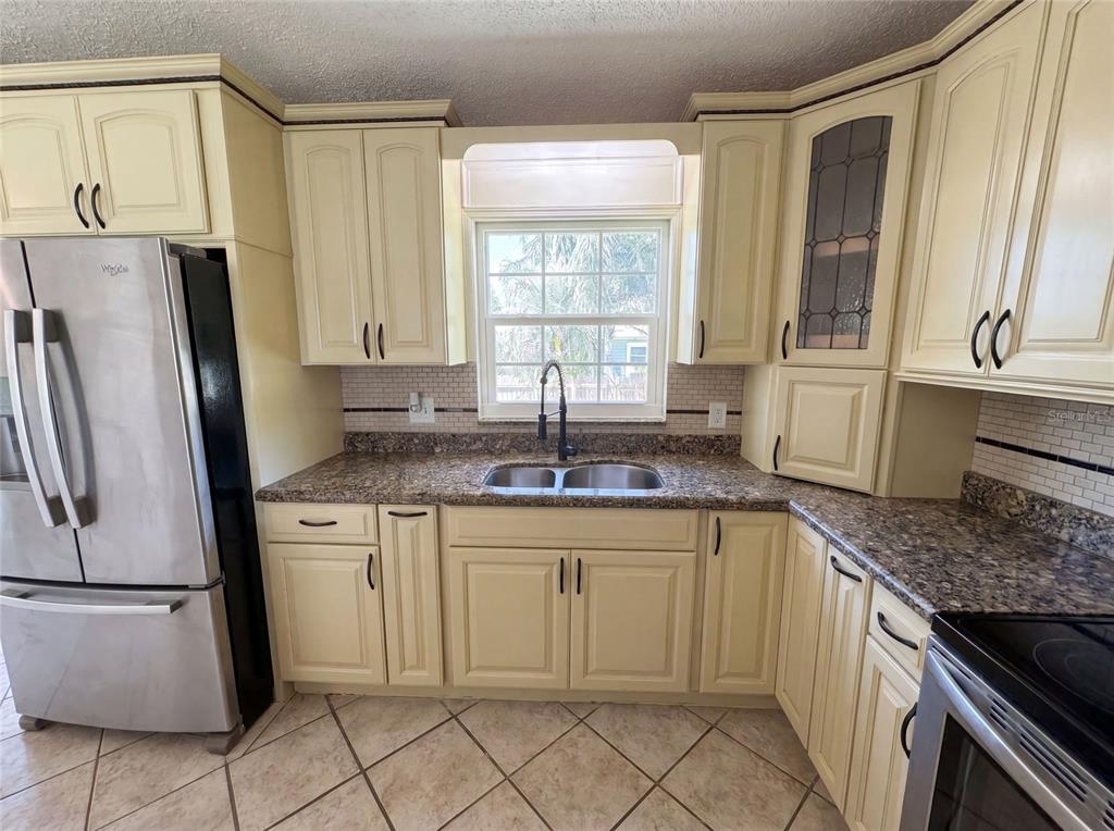 A kitchen features cream-colored cabinets, granite countertops, a stainless steel refrigerator, and a window — 7820 HIGHWAY A1A, MELBOURNE BEACH, FL