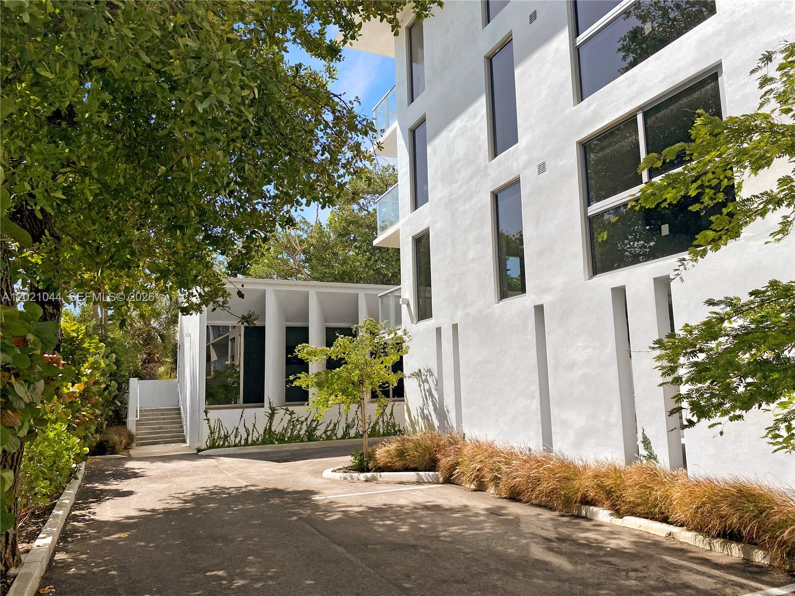 A modern white multi-story building stands next to a paved driveway and landscaped garden — 10250 Collins Avenue # 408, Bal Harbour FL 33154, BAL HARBOUR, FL