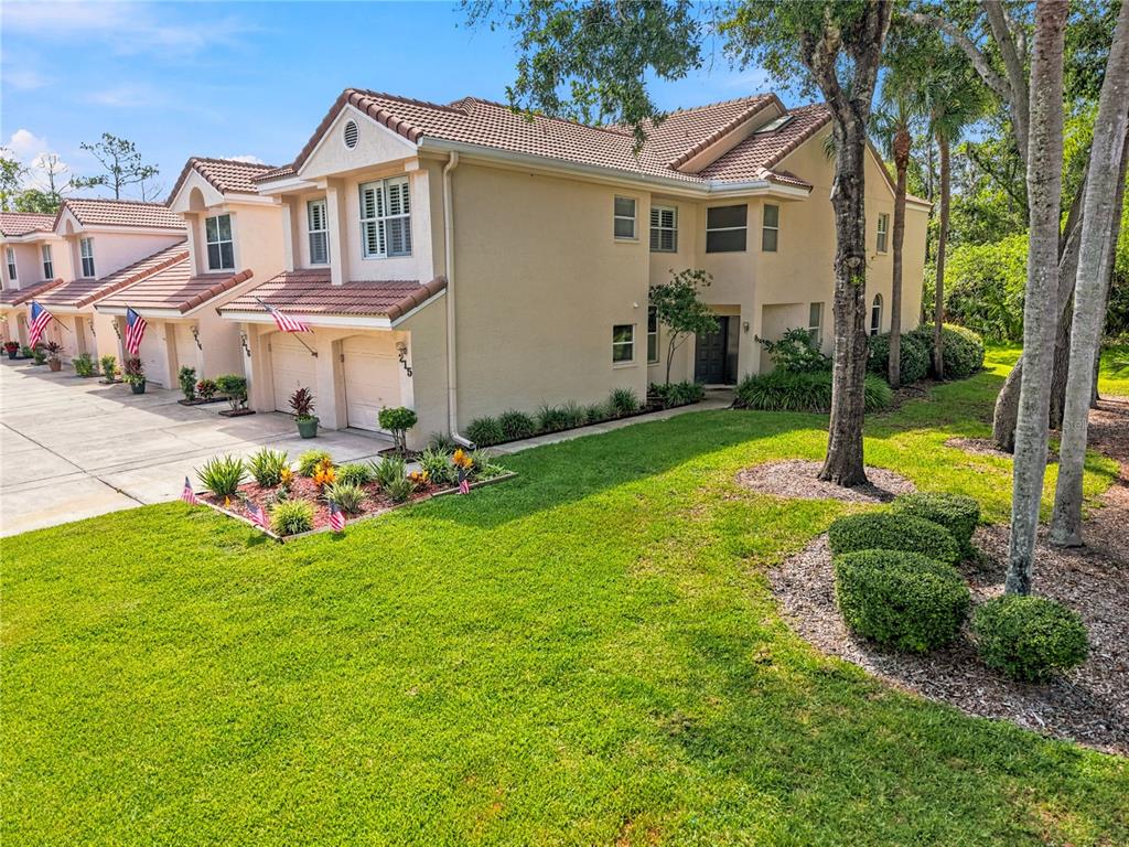 A two-story townhouse with a beige stucco exterior, a tiled roof, and a front lawn — 215 CLAYS TRAIL, OLDSMAR, FL