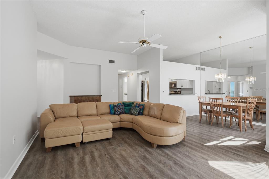 A living room with a tan sectional sofa, wood-look flooring, and an adjacent dining area — 215 CLAYS TRAIL, OLDSMAR, FL