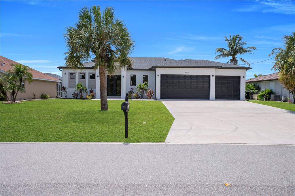 A single-story house with a white exterior, dark garage doors, and a palm tree in front — 4129 FLAMINGO BOULEVARD, PORT CHARLOTTE, FL