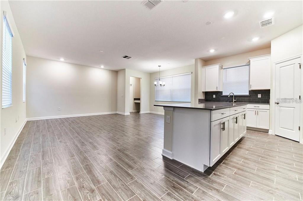 An open-concept kitchen and living area featuring white cabinets, a dark island, and wood-look flooring — 12027 GRAMMAR LANE, ORLANDO, FL