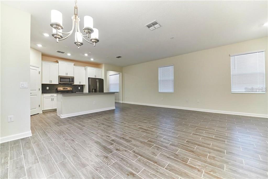 An open-concept kitchen and living area features white cabinetry, stainless steel appliances, and wood-look tile — 12027 GRAMMAR LANE, ORLANDO, FL