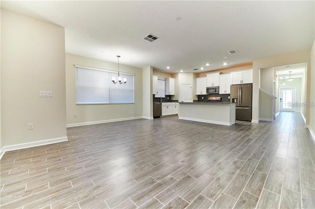 An open-concept kitchen and dining area features white cabinetry, stainless steel appliances, and wood-look flooring — 12027 GRAMMAR LANE, ORLANDO, FL