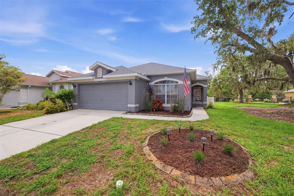 A gray single-story house with a two-car garage, arched window, and a circular garden bed — 9240 CREEDMOOR LANE, NEW PORT RICHEY, FL