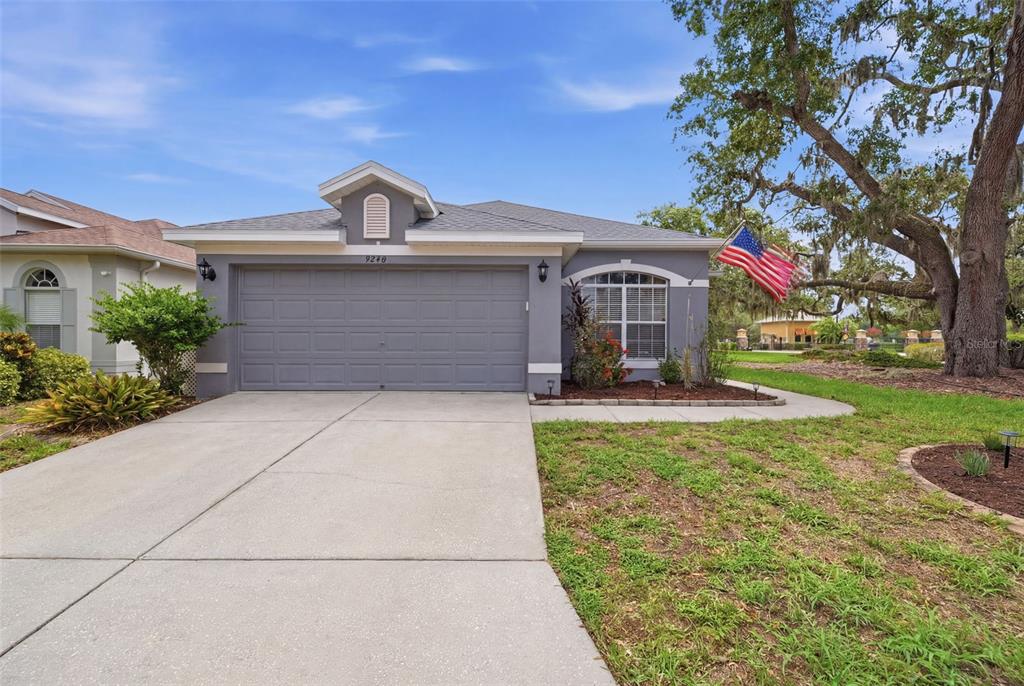 A gray single-story house with a two-car garage and a front yard at sunset — 9240 CREEDMOOR LANE, NEW PORT RICHEY, FL