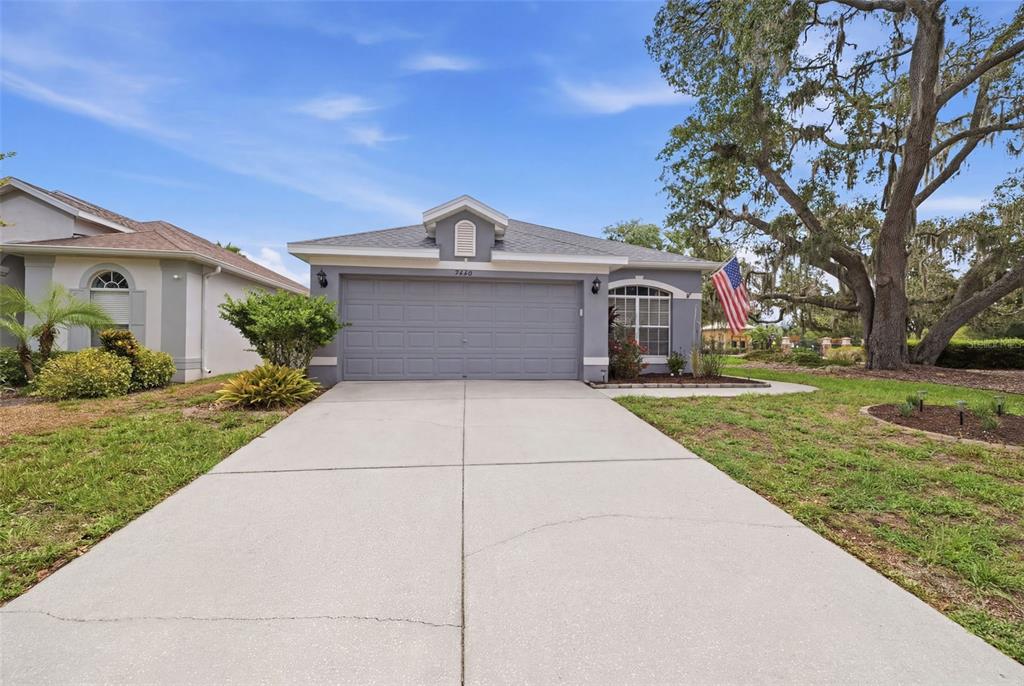 A single-story house with a gray garage, a concrete driveway, and a large oak tree — 9240 CREEDMOOR LANE, NEW PORT RICHEY, FL