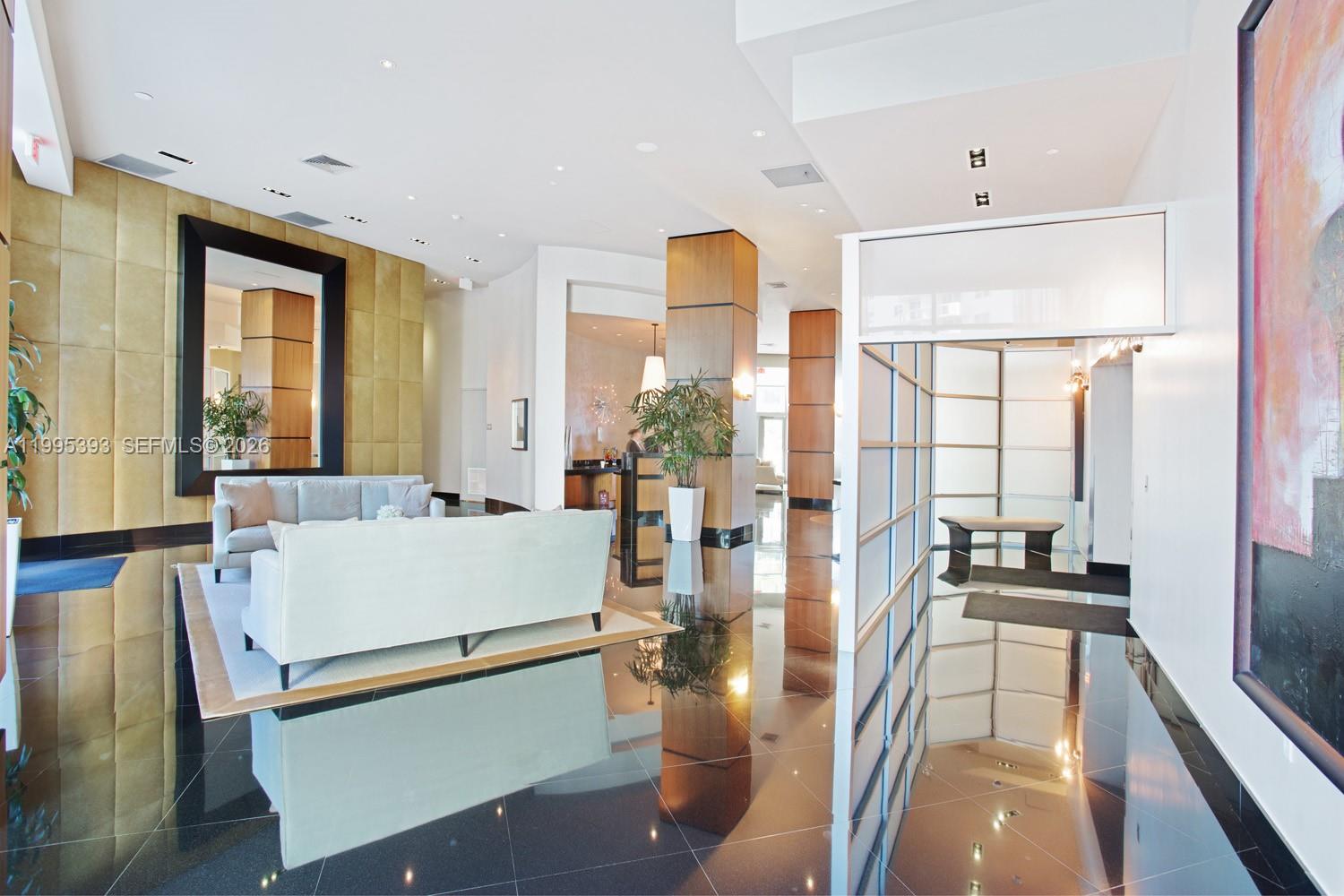 A modern lobby features a white sofa, a large mirror, and polished dark tile floors — 3101 S Ocean Dr # 1904, Hollywood FL 33019, HOLLYWOOD, FL