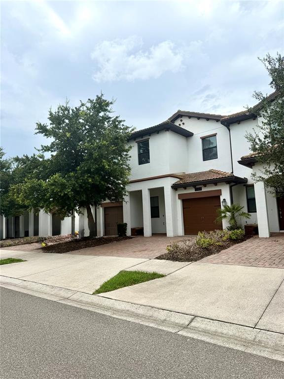 A two-story white townhouse features a brown garage door and a large tree in front — 1344 ROYAL ST GEORGE BOULEVARD, DAVENPORT, FL