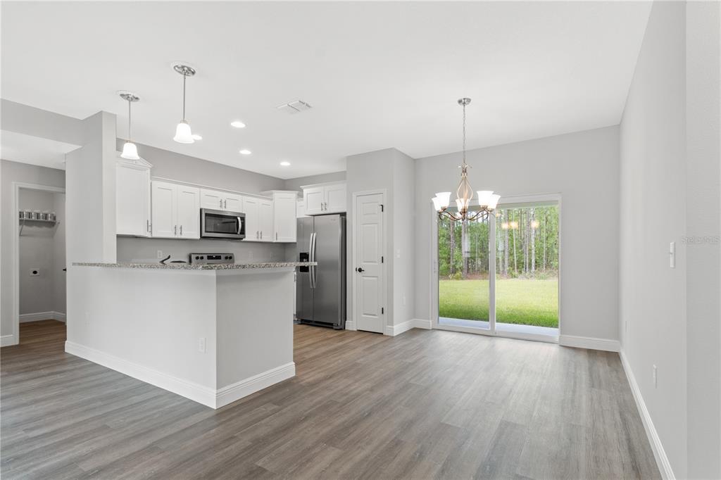 A kitchen and dining area feature white cabinets, stainless steel appliances, and wood-look flooring — 4372 MERCEDES STREET, SEBRING, FL