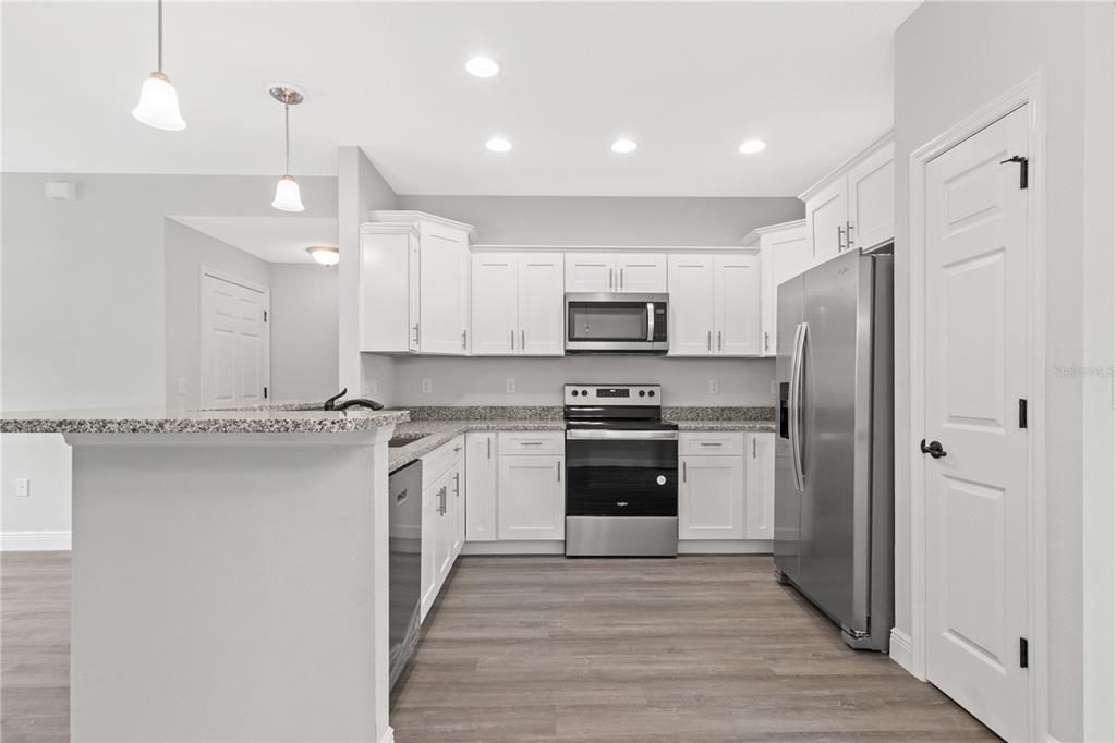 A kitchen features white cabinets, stainless steel appliances, granite countertops, and wood-look flooring — 4372 MERCEDES STREET, SEBRING, FL