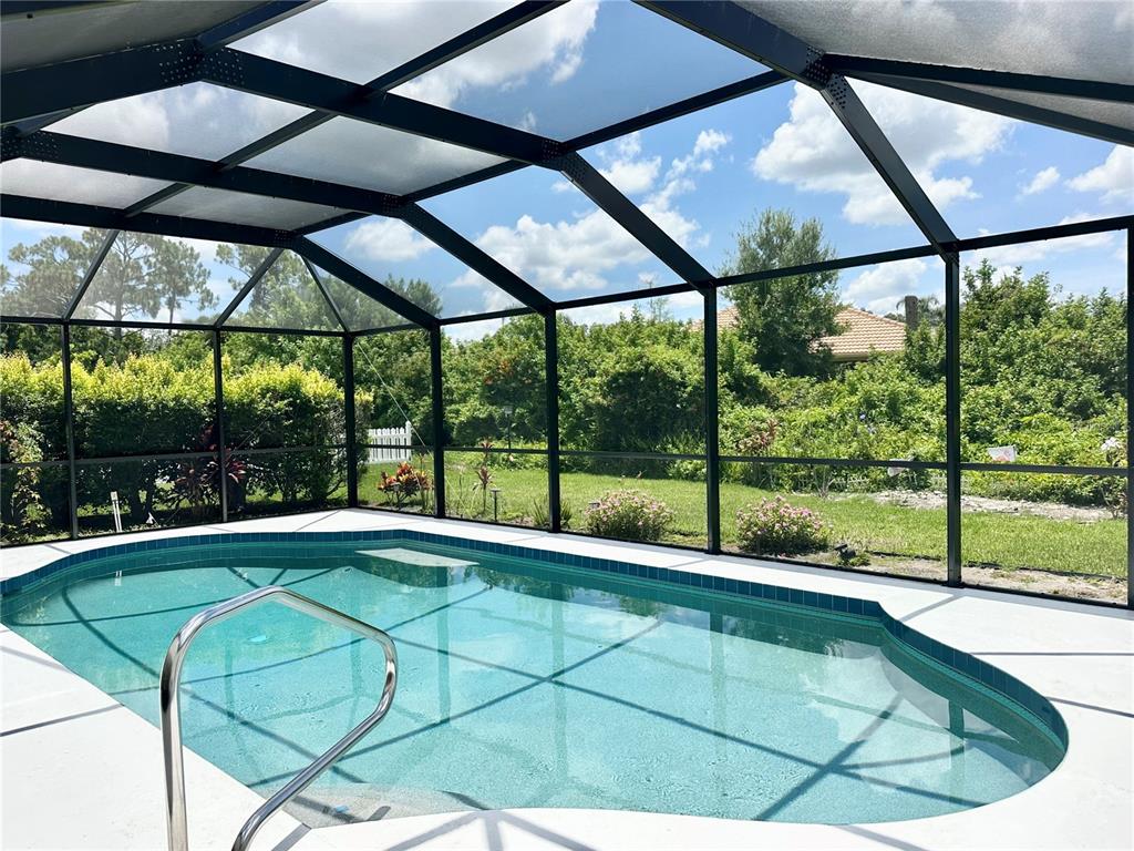 A screened-in swimming pool with a concrete deck overlooks a lush, green backyard — 5024 SOUTHERN PINE CIRCLE, VENICE, FL