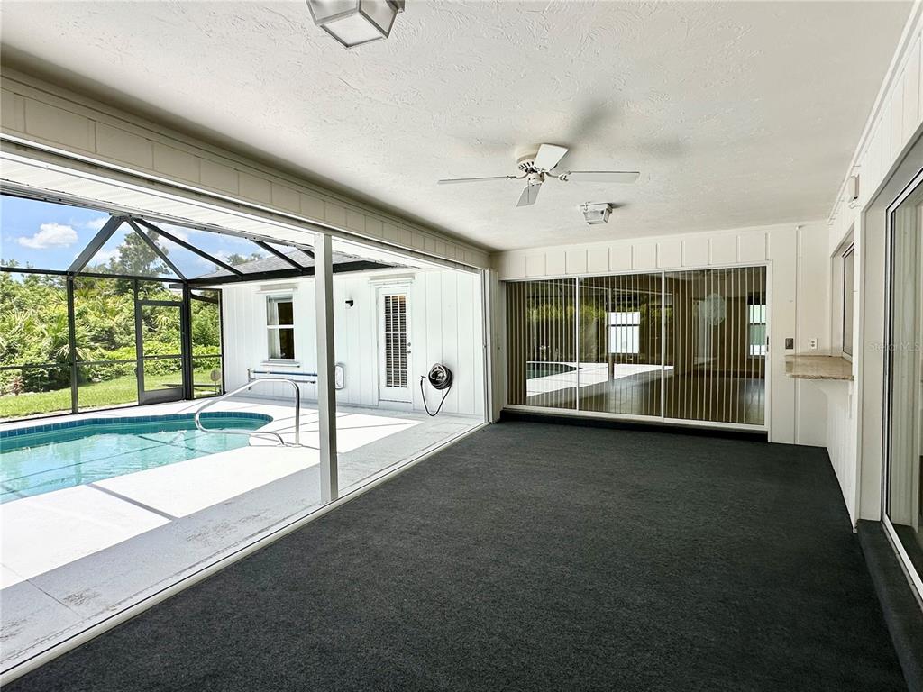 A covered patio with dark carpeting overlooks a swimming pool enclosed by a screen — 5024 SOUTHERN PINE CIRCLE, VENICE, FL