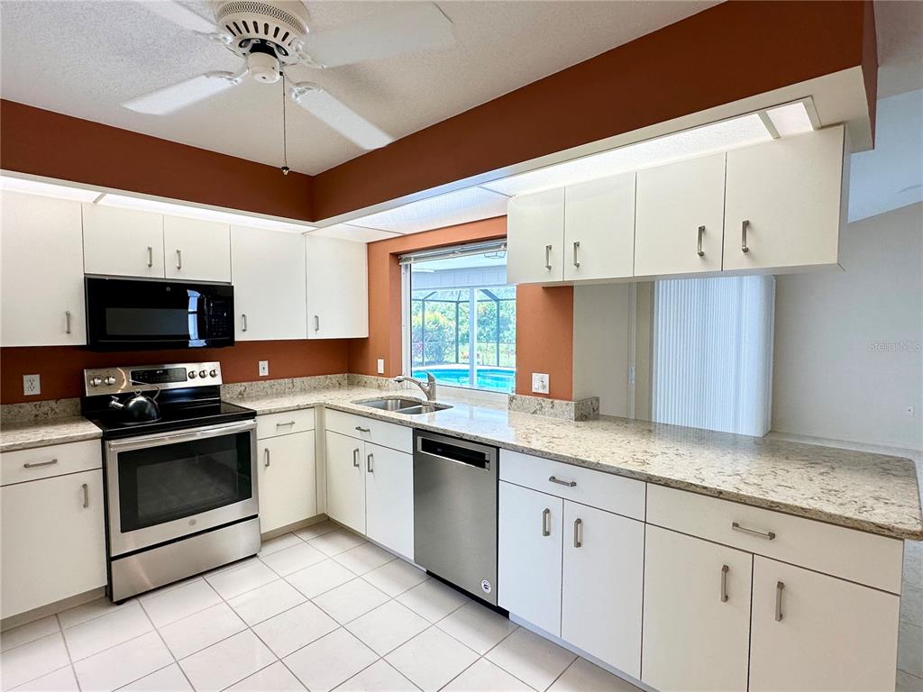 A kitchen with white cabinets, granite countertops, stainless steel appliances, and a view of a pool — 5024 SOUTHERN PINE CIRCLE, VENICE, FL