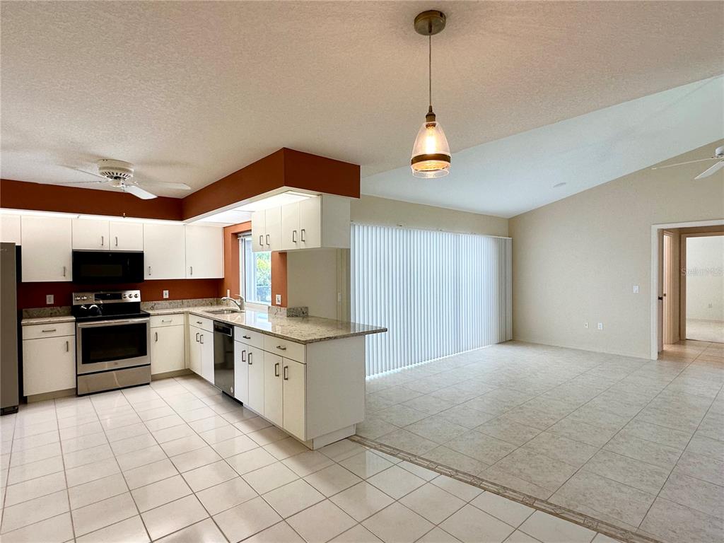 A kitchen with white cabinets and granite countertops opens into a tiled living area — 5024 SOUTHERN PINE CIRCLE, VENICE, FL