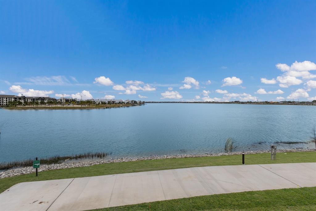 A concrete path overlooks a large lake with apartment buildings visible on the distant shore — 7420 NEWHAM LANE, SARASOTA, FL