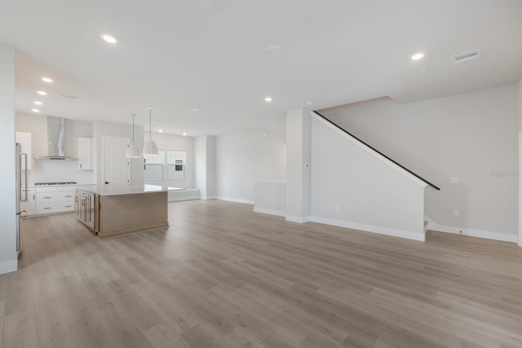An open-concept kitchen and living area features light wood flooring, white cabinetry, and a staircase — 7420 NEWHAM LANE, SARASOTA, FL