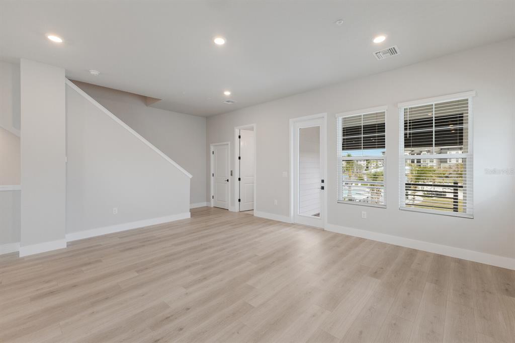 A bright living room features light wood-look flooring, white walls, recessed lighting, and two windows — 7420 NEWHAM LANE, SARASOTA, FL