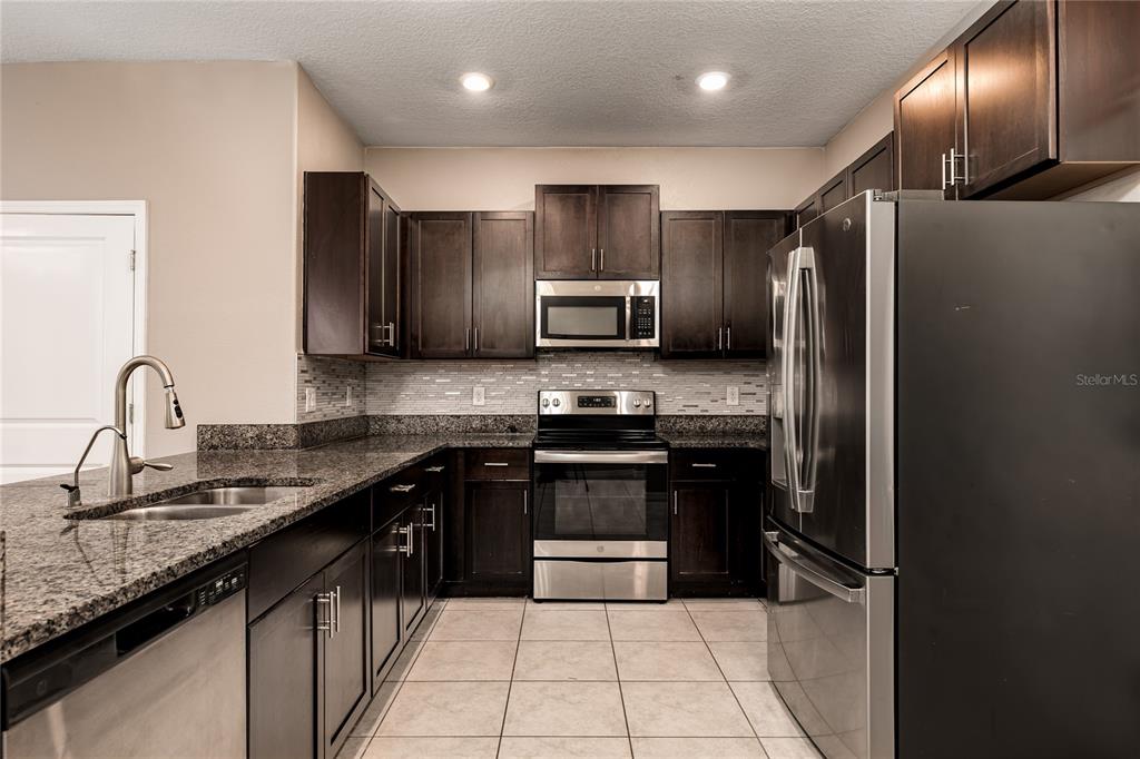 A kitchen features dark wood cabinets, granite countertops, stainless steel appliances, and tile flooring — 724 ROYAL EMPRESS DRIVE, RUSKIN, FL