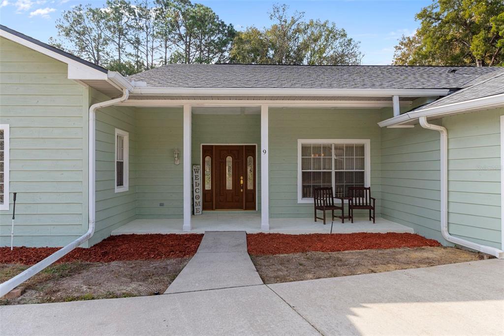A light green house exterior features a covered porch, a wooden front door, and chairs — 9 FOXGREEN COURT, HOMOSASSA, FL