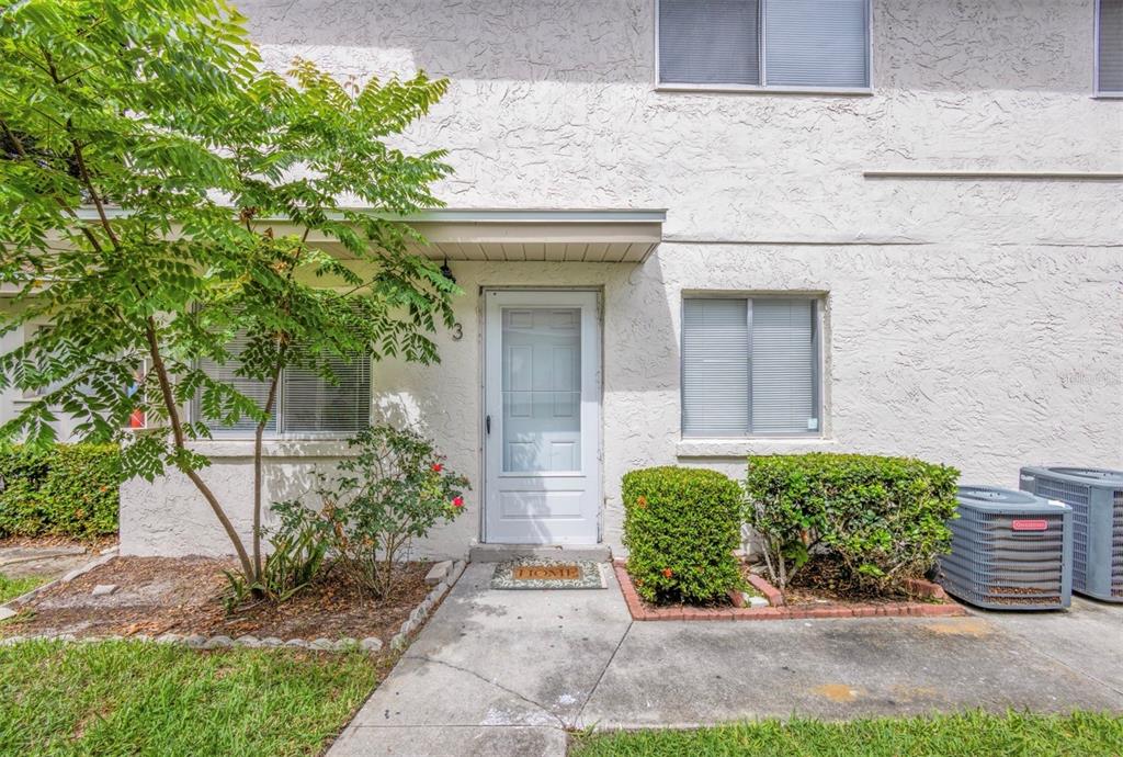 A white stucco townhouse exterior features a front door, two windows, and two air conditioning units — 1829 BOUGH AVENUE UNIT 3, CLEARWATER, FL