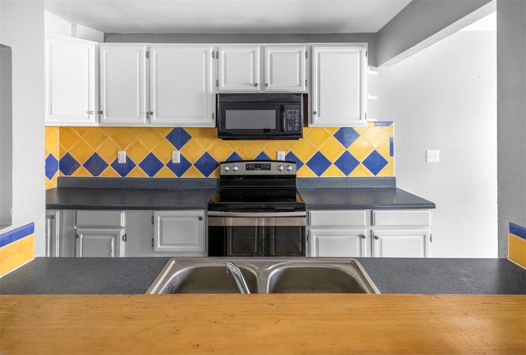 A kitchen features white cabinets, a dark countertop, and a yellow and blue tiled backsplash — 1829 BOUGH AVENUE UNIT 3, CLEARWATER, FL