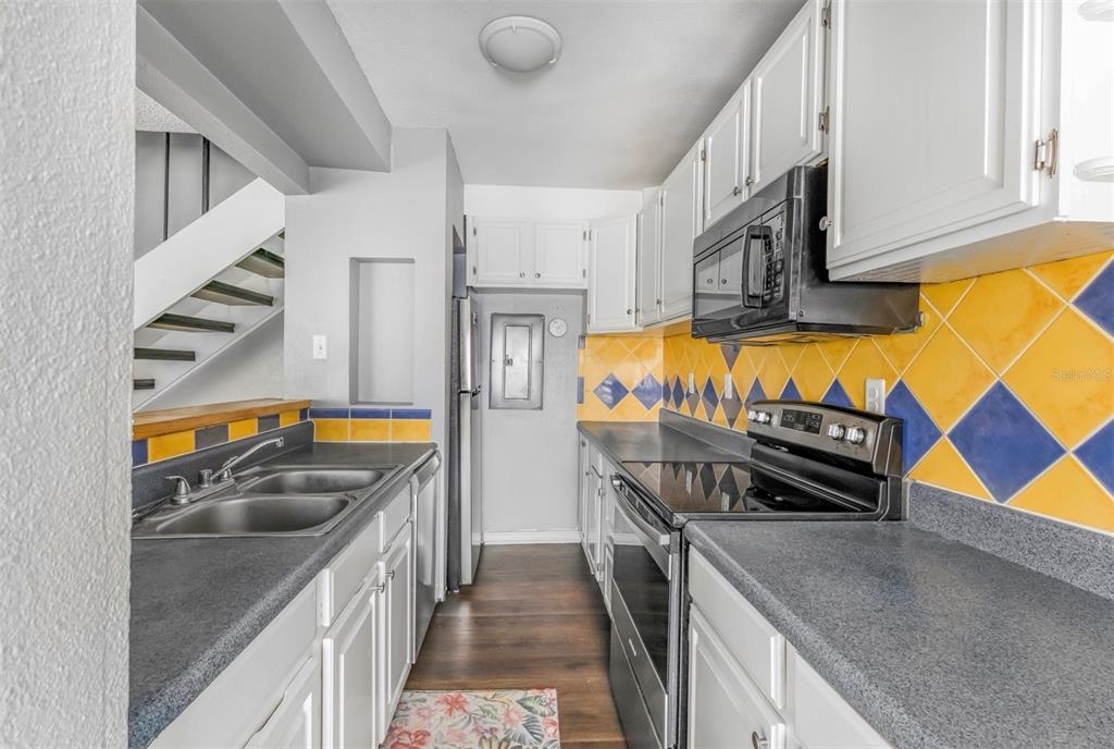 A galley kitchen features white cabinets, dark countertops, and a yellow and blue tiled backsplash — 1829 BOUGH AVENUE UNIT 3, CLEARWATER, FL