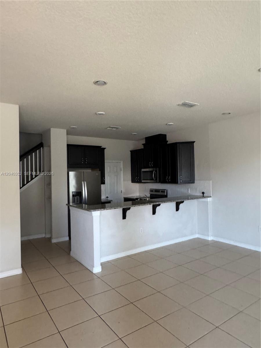 A kitchen features dark wood cabinets, stainless steel appliances, and a granite breakfast bar — 2713 Giardino Loop # 0, Kissimmee FL 34741, KISSIMMEE, FL