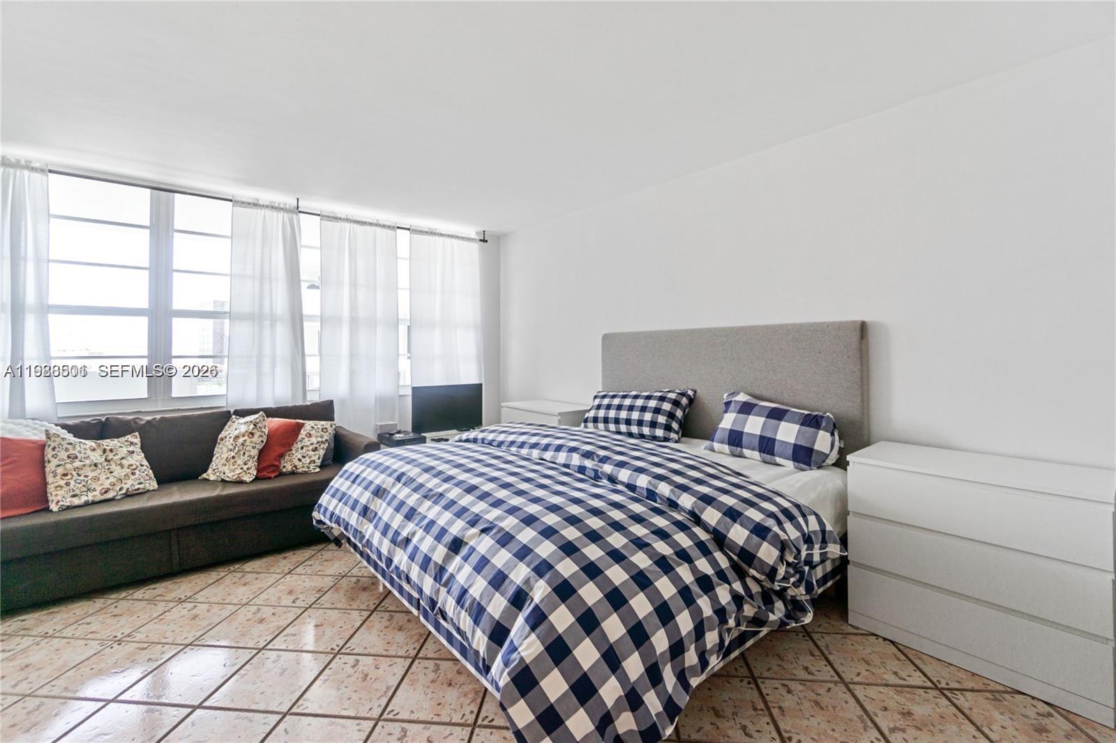 A bedroom features a checkered bed, a brown sofa, and light-colored tile flooring — 100 Lincoln Rd # 818, Miami Beach FL 33139, MIAMI BEACH, FL