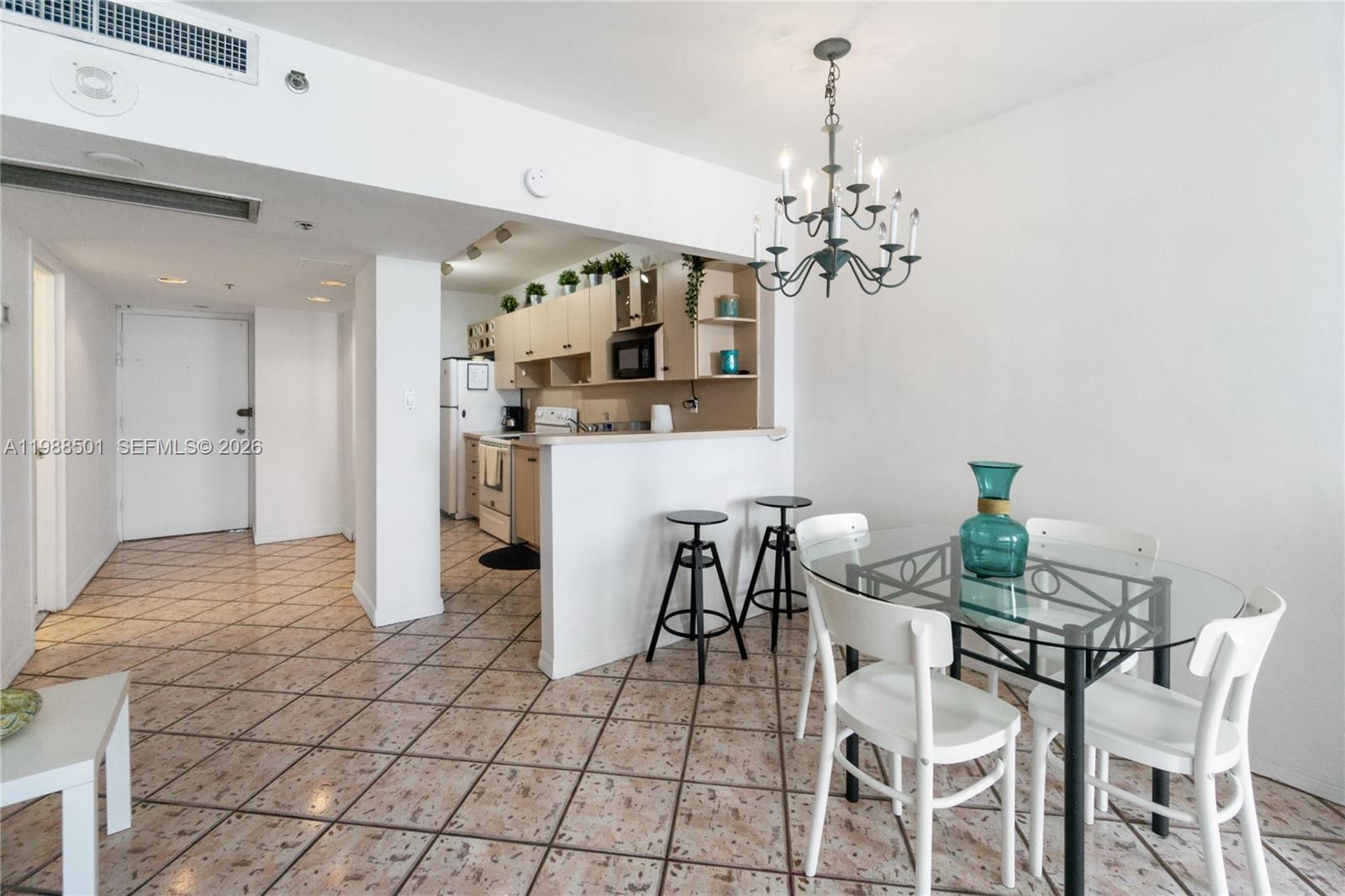 A dining area with a glass table and chandelier sits adjacent to a galley kitchen — 100 Lincoln Rd # 818, Miami Beach FL 33139, MIAMI BEACH, FL