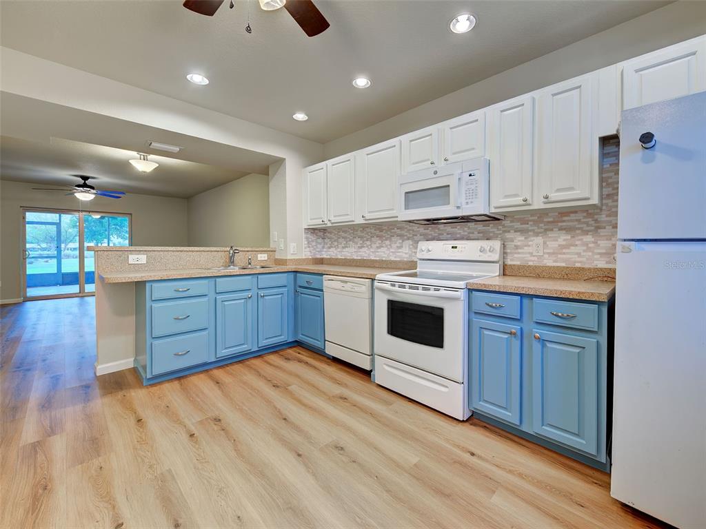 A kitchen features blue lower cabinets, white upper cabinets, and light wood-look flooring — 26396 NADIR ROAD UNIT 506, PUNTA GORDA, FL