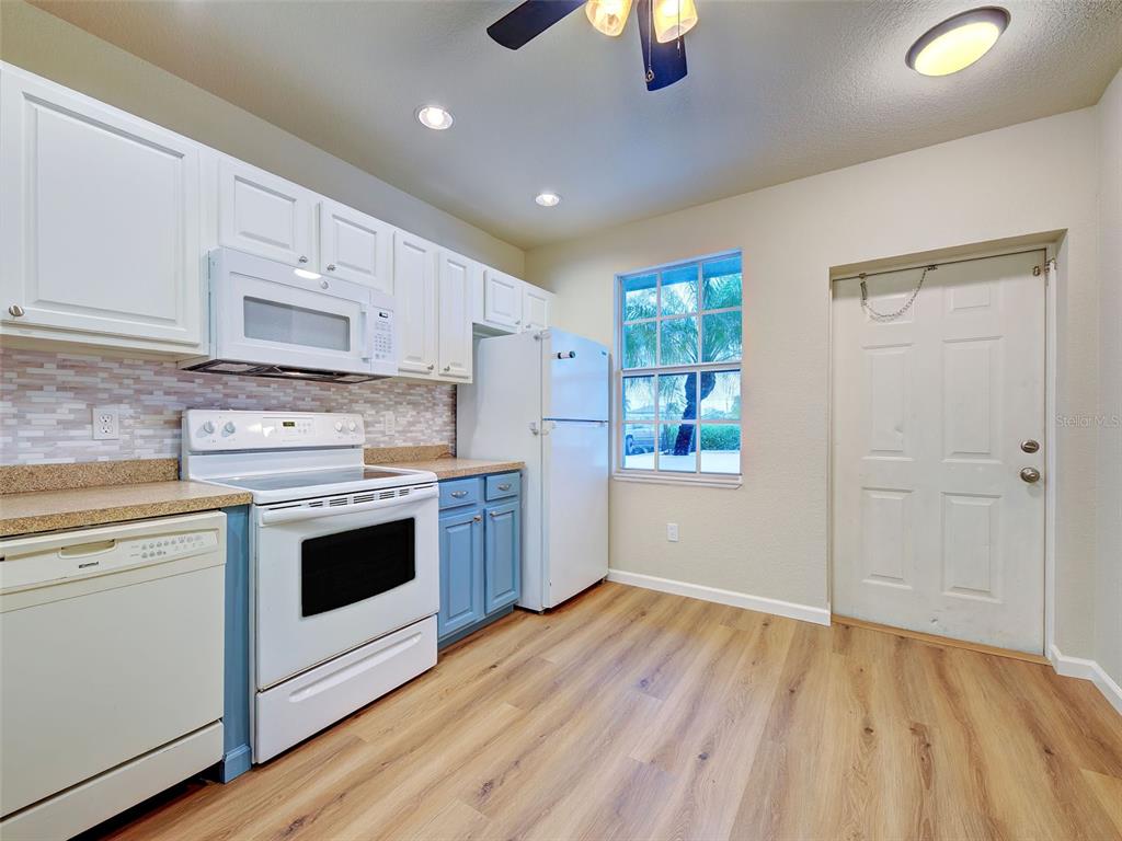 A kitchen features white upper cabinets, blue lower cabinets, white appliances, and light wood flooring — 26396 NADIR ROAD UNIT 506, PUNTA GORDA, FL
