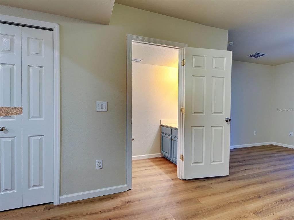 A room with wood-look flooring, a white closet door, and an open doorway to a bathroom — 26396 NADIR ROAD UNIT 506, PUNTA GORDA, FL