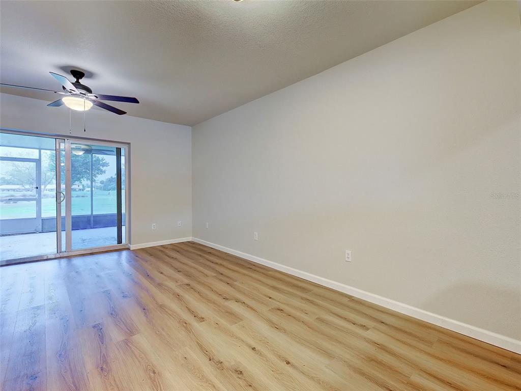 An empty room features light wood-look flooring, a ceiling fan, and sliding glass doors — 26396 NADIR ROAD UNIT 506, PUNTA GORDA, FL