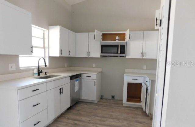A kitchen features white cabinets, light countertops, stainless steel appliances, and wood-look flooring — 705 SW 9TH COURT, CAPE CORAL, FL