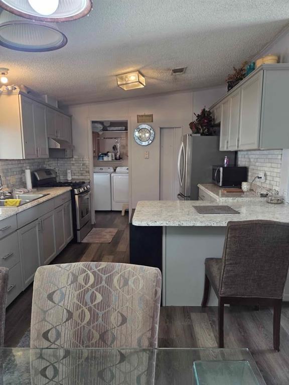 A kitchen features gray cabinetry, a white tiled backsplash, a kitchen island, and stainless steel appliances — 1400 ROBINSON CIRCLE UNIT 111, FORT MEADE, FL