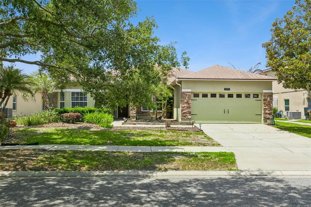 A single-story house with a green garage door, stone accents, and a large front tree — 237 STRATHMORE CIRCLE, KISSIMMEE, FL