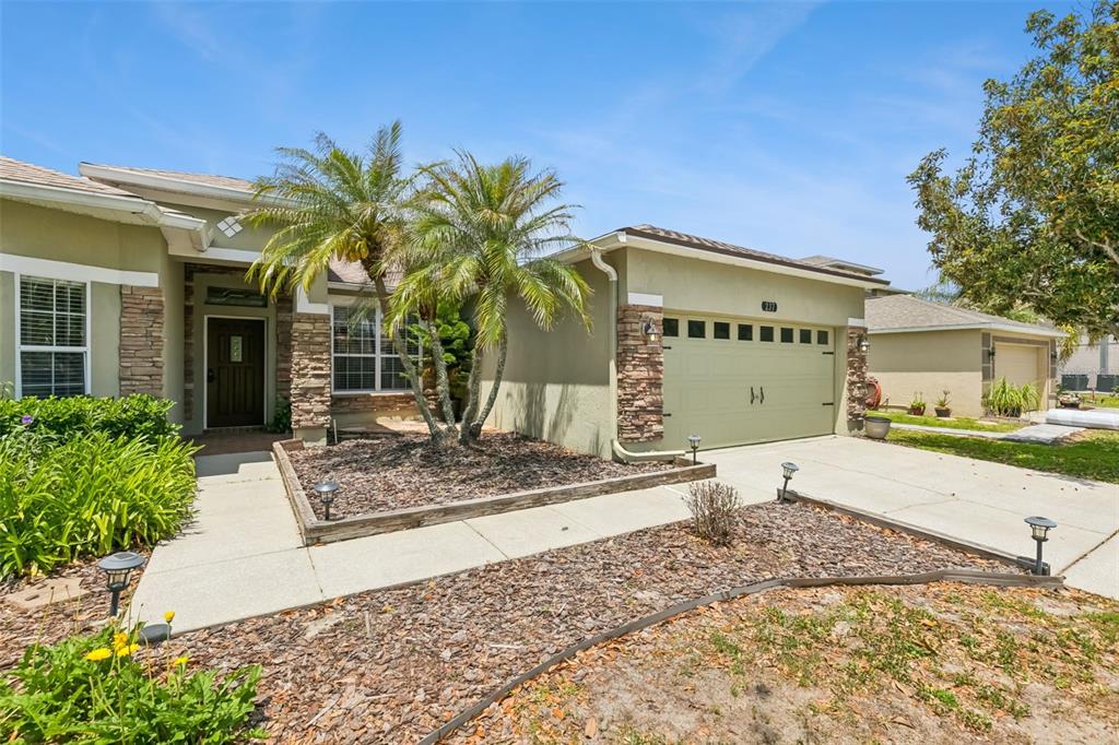 A single-story house with a tan stucco exterior, stone accents, and a palm tree garden — 237 STRATHMORE CIRCLE, KISSIMMEE, FL