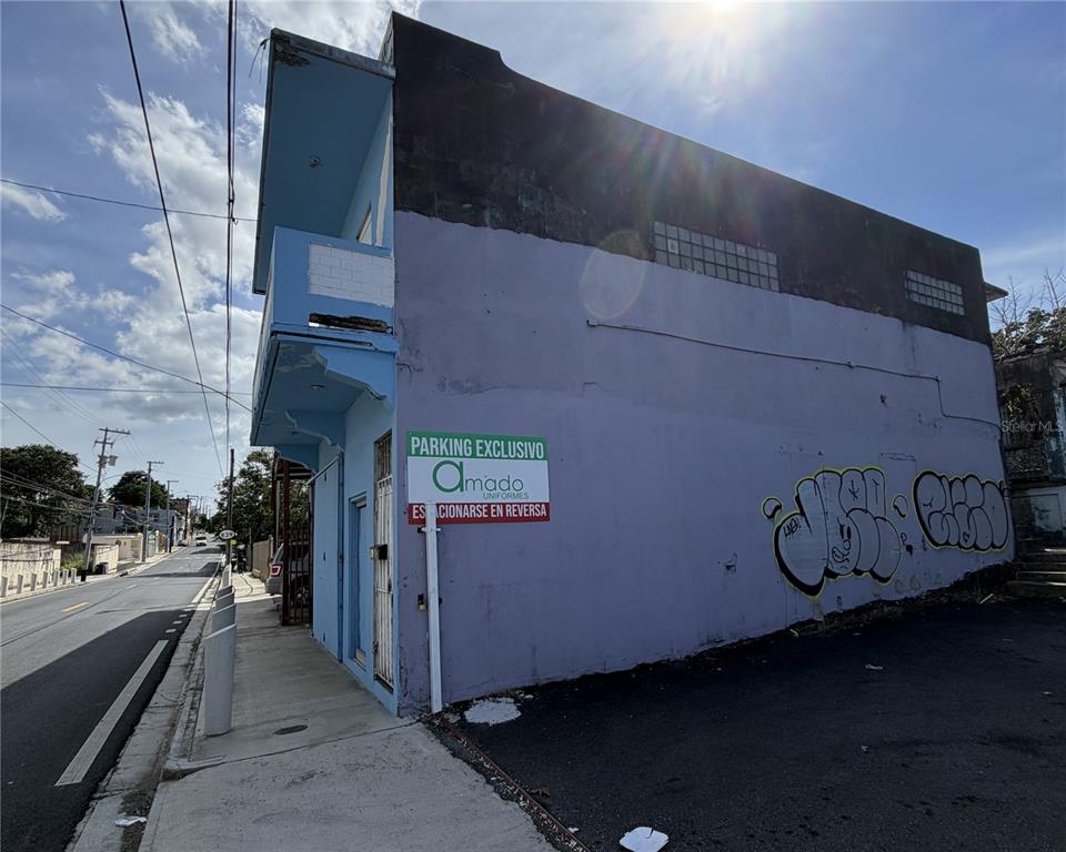 A light blue two-story building features a parking sign and graffiti on its side wall — 839 C. HIRAM GONZÁLEZ, BAYAMON, PR