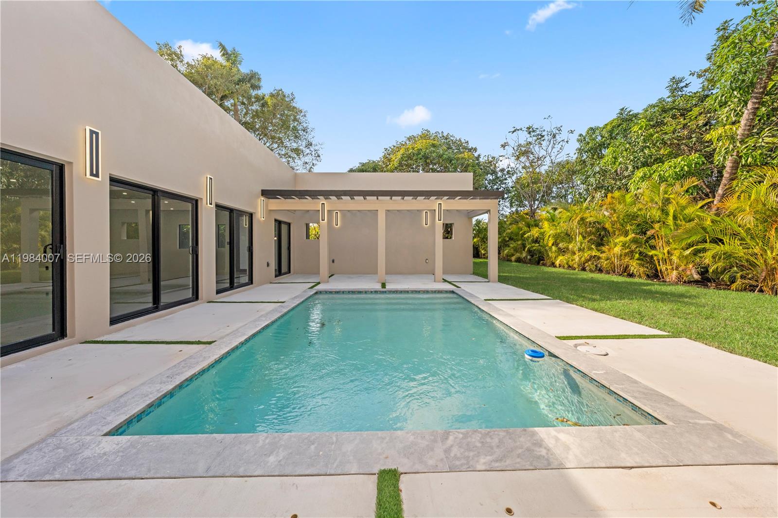 A rectangular swimming pool sits on a concrete patio beside a modern house with a pergola — 12335 Griffing Blvd, North Miami FL 33161, NORTH MIAMI, FL