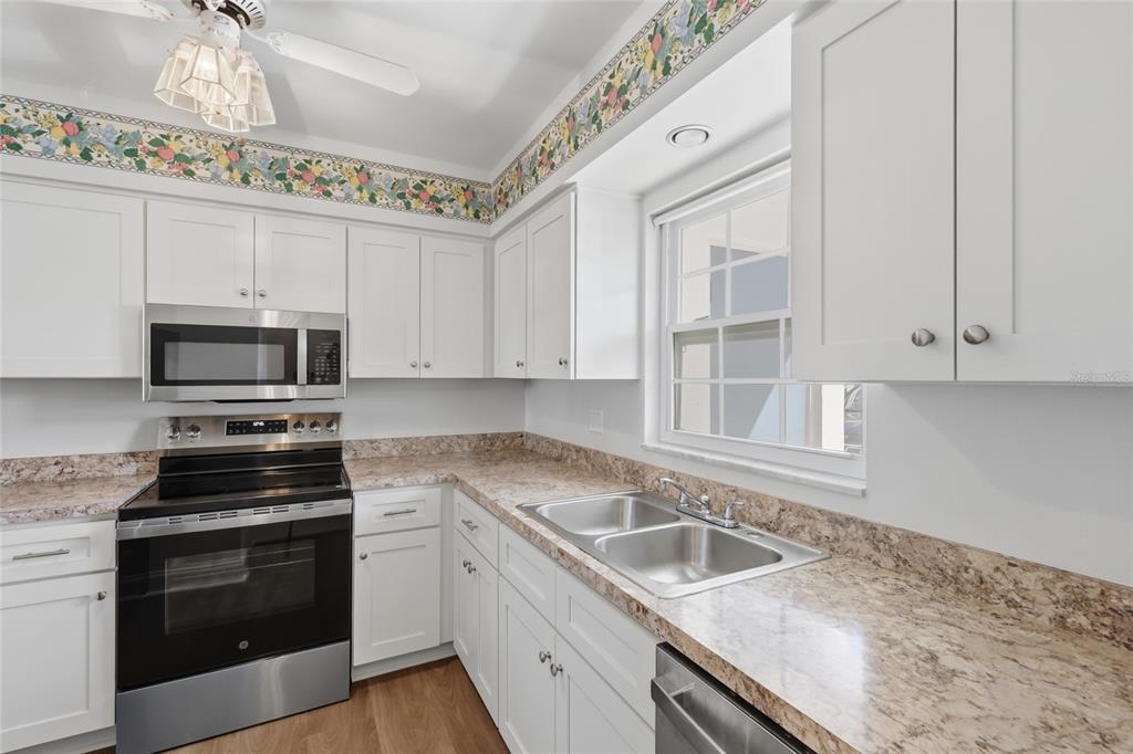 A kitchen with white cabinets, stainless steel appliances, laminate countertops, and floral wallpaper border — 9917 DESOTO COURT UNIT 9917, BRADENTON, FL