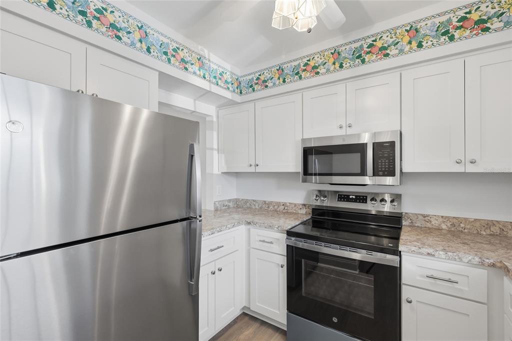 A kitchen features white cabinets, stainless steel appliances, granite-look countertops, and a floral wallpaper border — 9917 DESOTO COURT UNIT 9917, BRADENTON, FL