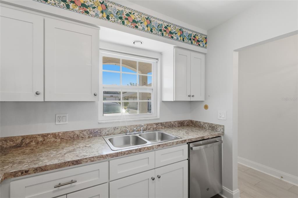 A kitchen features white cabinets, a double-basin sink, granite countertops, and a floral wallpaper border — 9917 DESOTO COURT UNIT 9917, BRADENTON, FL