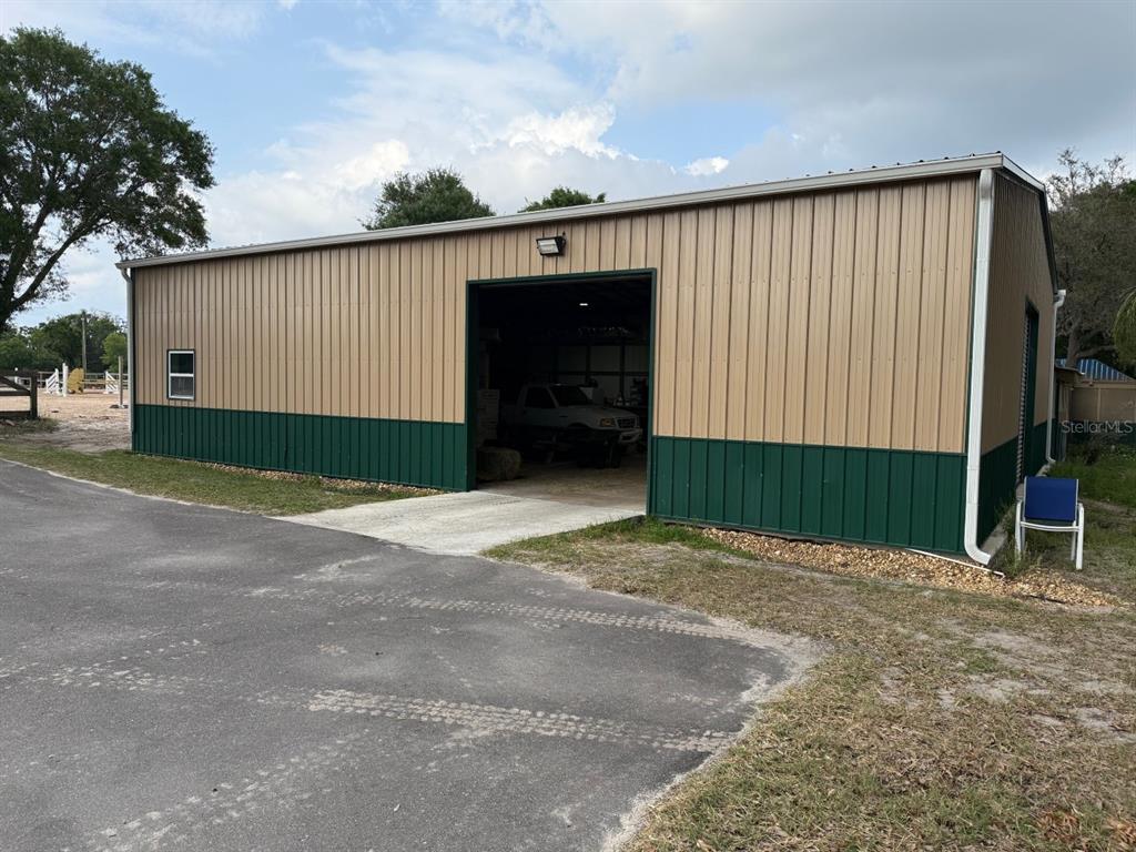 A metal workshop building with tan and green siding stands next to a paved driveway — 16315 MCGLAMERY ROAD, ODESSA, FL