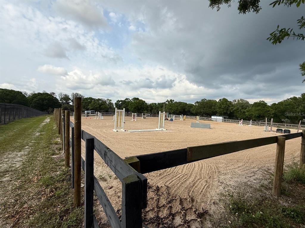 An outdoor horse riding arena with jumps, enclosed by a wooden fence under a cloudy sky — 16315 MCGLAMERY ROAD, ODESSA, FL
