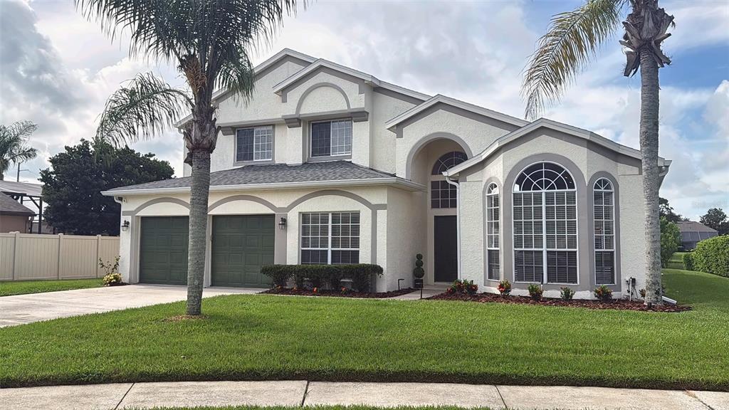 A two-story house with a light-colored stucco exterior, green garage doors, and two palm trees — 2361 MID PINE COURT, OVIEDO, FL