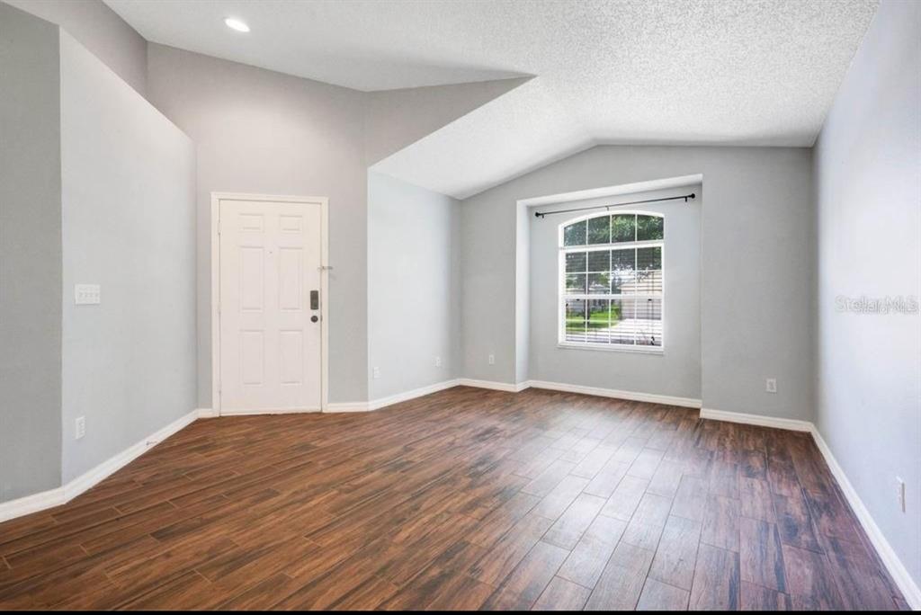 An empty room with light gray walls, vaulted ceilings, and dark wood-look plank flooring — 14795 YORKSHIRE RUN DRIVE, ORLANDO, FL