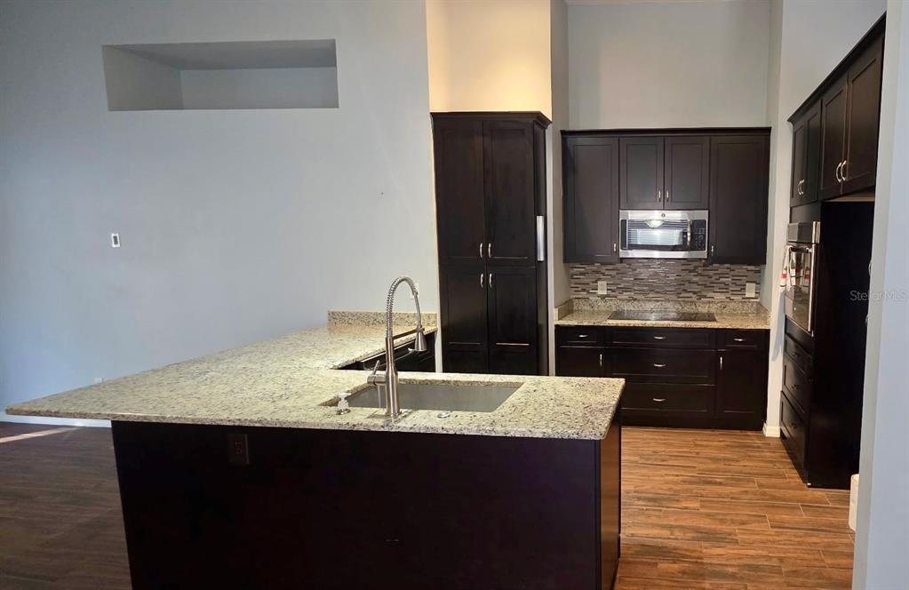 A kitchen features dark wood cabinets, granite countertops, a center island with a sink, and tile flooring — 14795 YORKSHIRE RUN DRIVE, ORLANDO, FL
