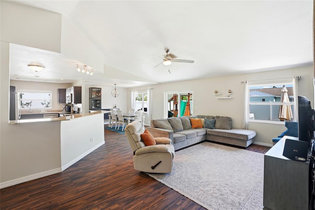 An open-concept living and dining area features wood-look flooring, a sectional sofa, and kitchen access — 8405 SOMERSET DRIVE, LARGO, FL